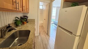 A kitchen with wooden cabinets, a stainless steel sink, a white refrigerator, and a potted plant on the countertop. - Relaxing Kalakauan 1-Bedroom | Recently Redecorated! (Honolulu)