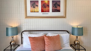 A neatly made bed with two pillows, a framed picture above it, and two bedside lamps on either side. - Relaxing Kalakauan 1-Bedroom | Recently Redecorated! (Honolulu)