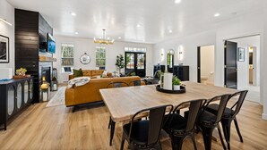 Een moderne woonkamer met een houten eettafel, zwarte stoelen, een bank en een open haard.