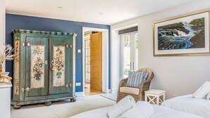 A bedroom with a bed, a wicker chair, a painting, and a vintage cabinet. - Charming Cottage with Garden - Pass the Keys (Chichester)