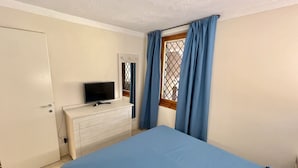A bedroom with a bed, a dresser, a television, and a window with curtains.