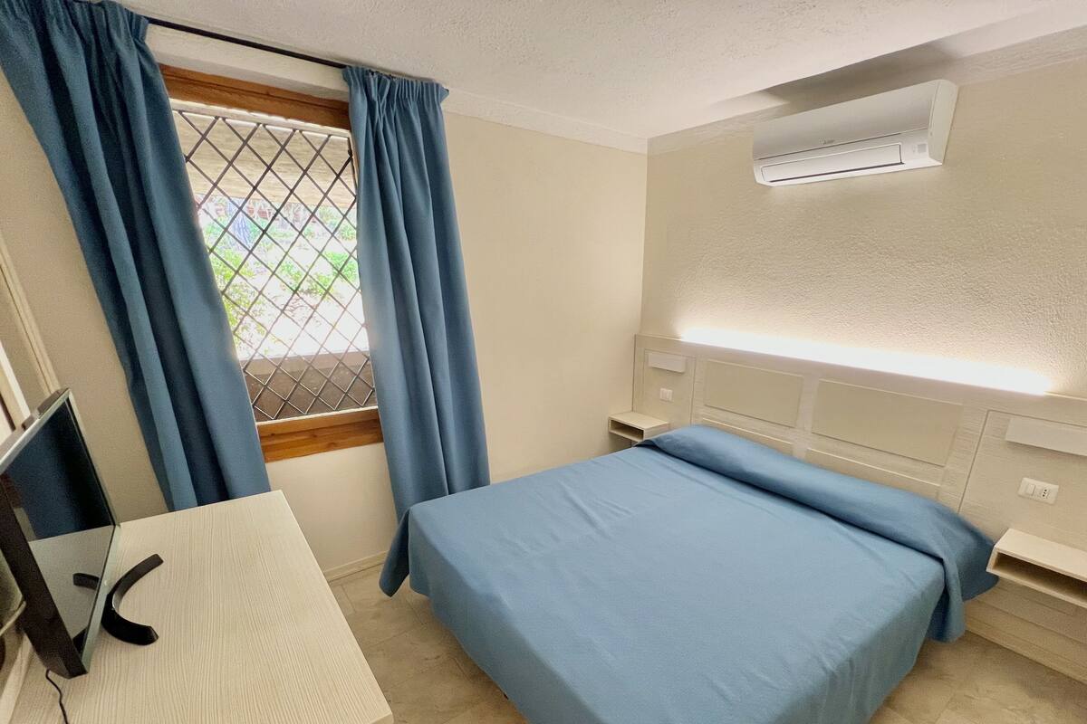 Ein Hotelzimmer mit Bett, Schreibtisch, Stuhl und einem Fenster mit Vorhängen.