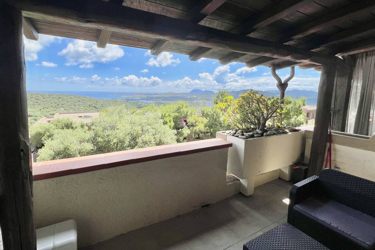 Ein Balkon mit Blick auf eine Berglandschaft, einem Blumentopf und einem Korbsessel.