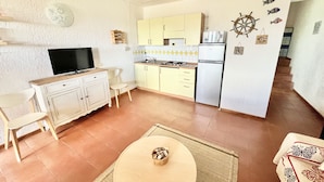 A compact kitchen with a TV, dining table, and chairs, and a small dining area with a rug.