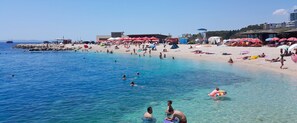 A beach with clear blue water, people swimming and sunbathing, and beach umbrellas.