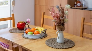 Een houten eettafel met een schaal fruit, een vaas met gedroogde bloemen en een rode pot.
