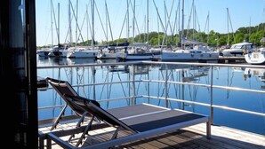 Un port de plaisance où sont amarrés de nombreux voiliers, une terrasse couverte avec des fauteuils et une vue dégagée sur l’eau.