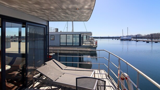A modern deck with lounge chairs, a glass-enclosed area, and a view of the marina with boats.