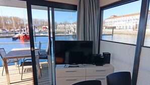 A room with a TV, a desk, and a view of a marina with boats and buildings.