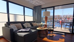 A modern living room with a dark grey sofa, a round coffee table, and a view of a marina through large windows.