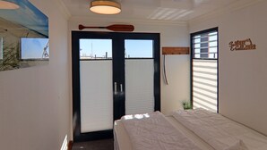 A bedroom with a bed, a wooden paddle on the ceiling, a window with blinds, and a wall sign.