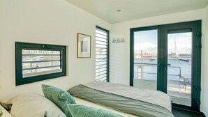 A bedroom with a bed, a window, and a door leading to a balcony with a view of the water. - Hausboot in Boltenhagen (Boltenhagen)
