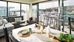 A modern dining area with a table set for two, large windows offering a view of a marina with boats. - Hausboot in Boltenhagen (Boltenhagen)