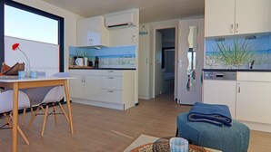 A modern kitchen with white cabinets, a dining area with a wooden table and chairs, and a view of the outdoors through a large window.