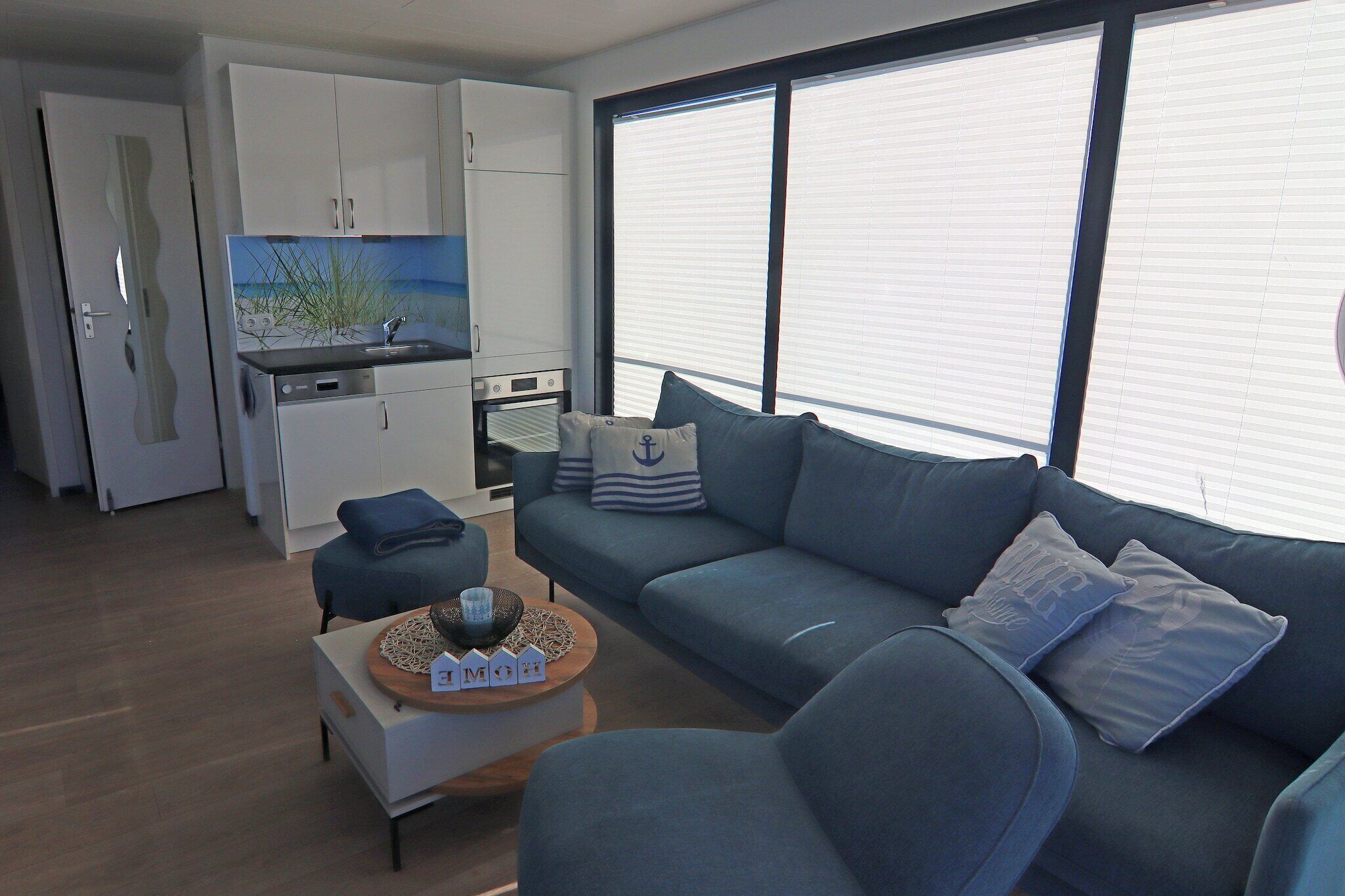 Een moderne woonkamer met een bank, salontafel en een keuken met witte kastjes en een inbouwoven.