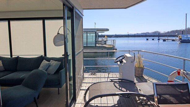 A modern balcony with a sofa, a dining table, and a view of the water.