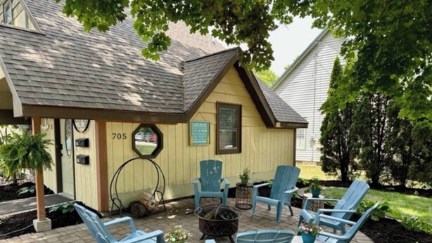 A patio with blue chairs and tables, a small shed with the number 705, and a tree providing shade. - Cottage Daze (Clear Lake)