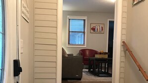 A staircase leading to a living room with a red couch, a window with blinds, and a small table with a yellow object. - Cottage Daze (Clear Lake)