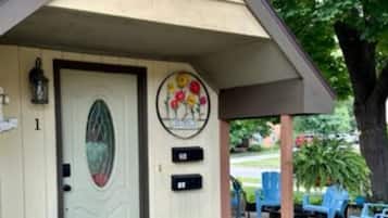 Welcome to a charming entrance with a green door, flanked by garden beds and a patio area with seating.