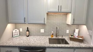 A kitchen with grey cabinets, a granite countertop, a stainless steel sink, and a dishwasher. - Cottage Daze (Clear Lake)