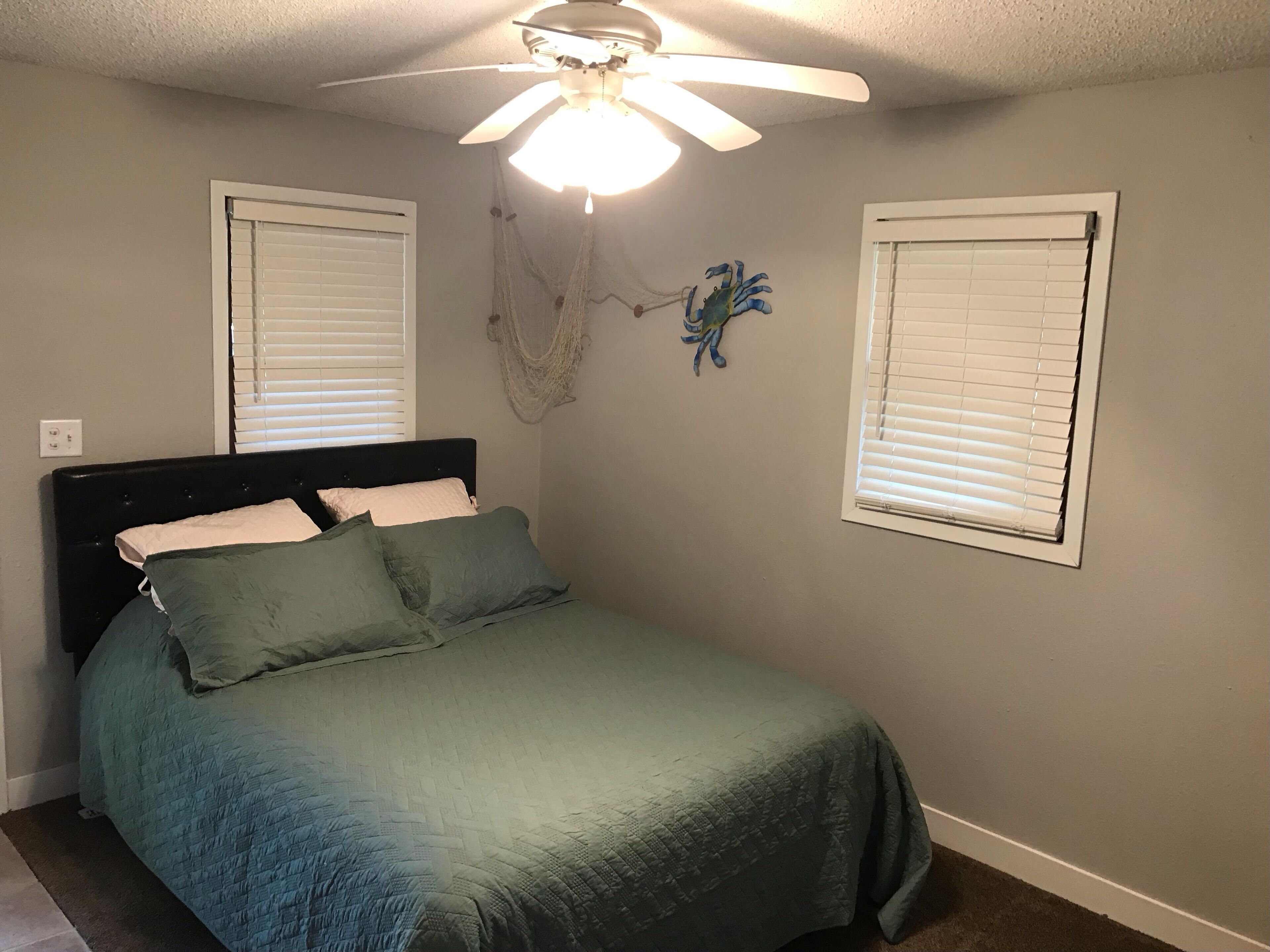A bedroom with a bed, a ceiling fan, and two windows with blinds.
