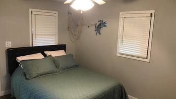 A bedroom with a bed, a ceiling fan, and two windows with blinds.