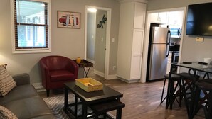 A living room with a red chair, a gray sofa, and a coffee table. There is a kitchen area with a refrigerator and a dining table with chairs. - Cottage Daze (Clear Lake)