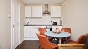 A compact kitchen with white cabinets, a stainless steel range hood, and a round table with orange chairs. - The Holland Park Crib - Classy 2bdr House (London)