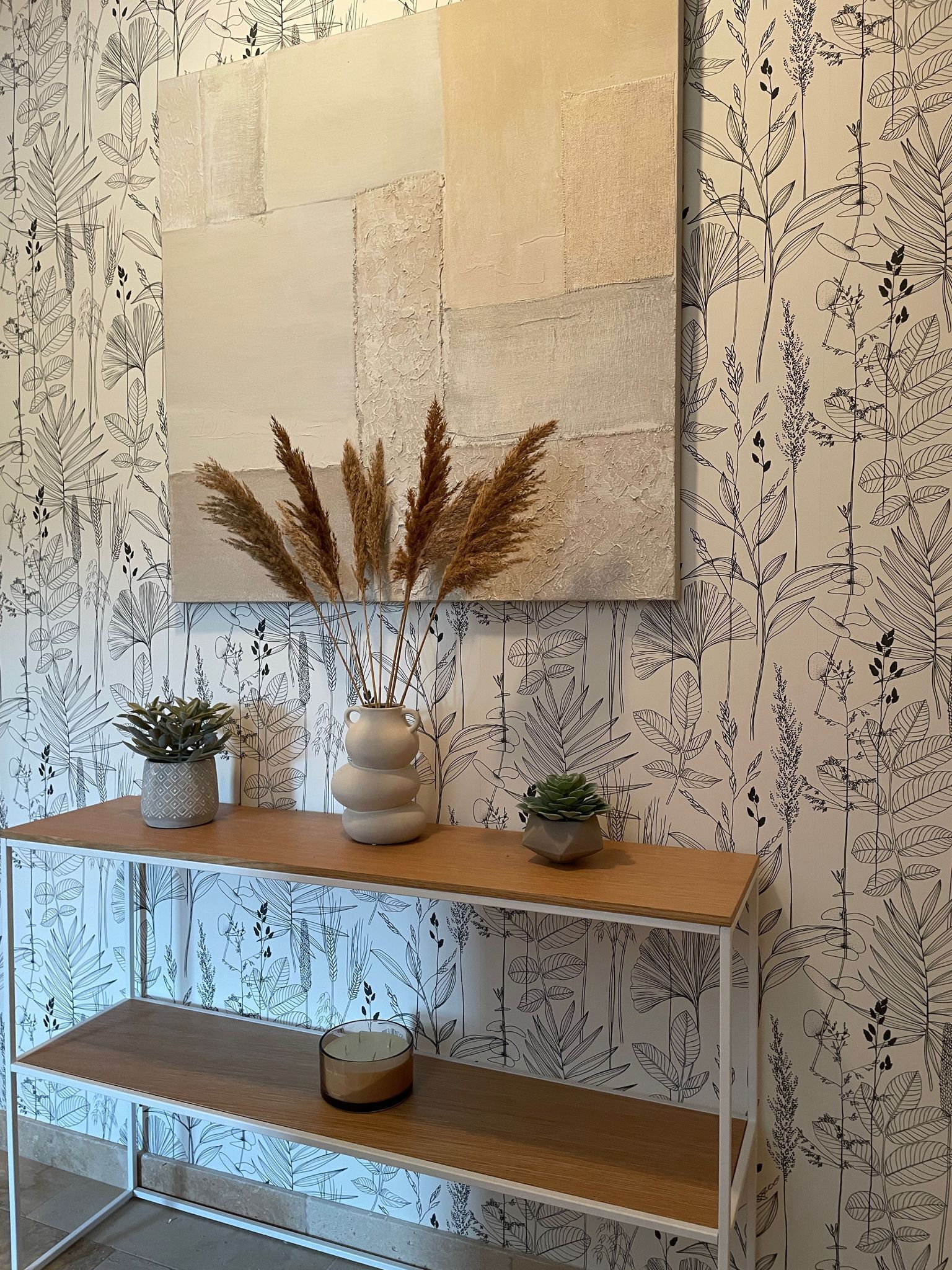 Une console en bois ornée de trois plantes en pot et d’une œuvre d’art accrochée au mur.