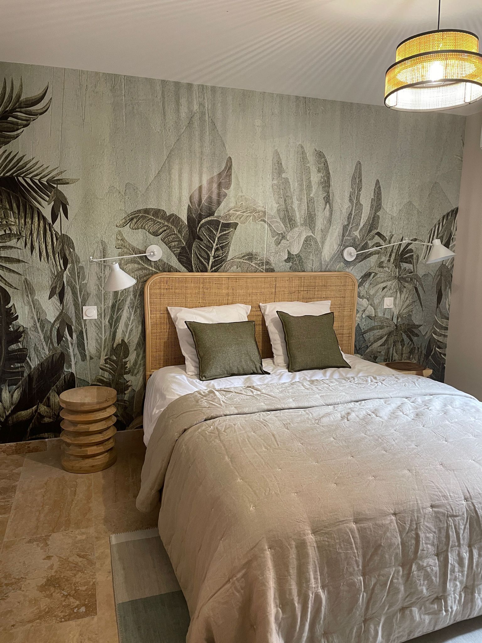 Une chambre à coucher comprenant un lit, une tête de lit en rotin, une fresque murale, une lampe de chevet et une lampe sur pied.