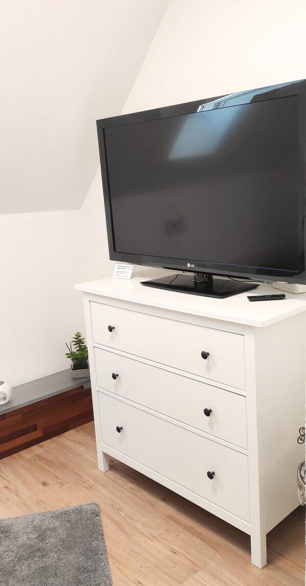 A white TV stand with a flat-screen TV, a remote control, and a small sign. - Cozy apartment with an outdoor terrace and barbecue between the Taunus and Spessart regions (Schöneck)