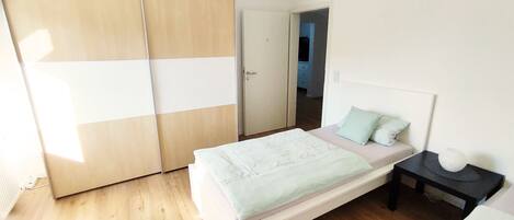 A bedroom with a bed, a nightstand, a wardrobe, and a door leading to another room.