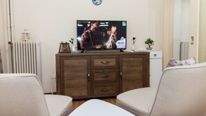 A living room with a television on a wooden cabinet, two beige sofas, a radiator, and a small potted plant. - Cozy Cute apt next to Agios Nikolaos (Athens)