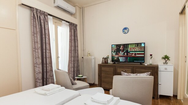 A hotel room with two beds, a TV, a small table with a flower, and a radiator. - Cozy Cute apt next to Agios Nikolaos (Athens)