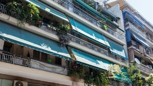 A multi-story building with balconies, a shop on the ground floor, and parked cars. - Cozy Cute apt next to Agios Nikolaos (Athens)