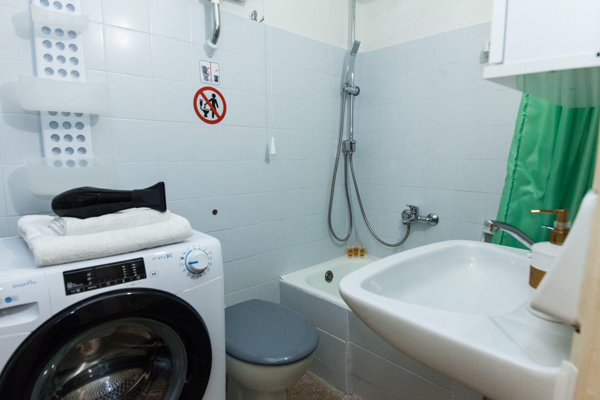 Une petite salle de bain équipée d’un lave-linge, de toilettes, d’une douche et d’un lavabo.
