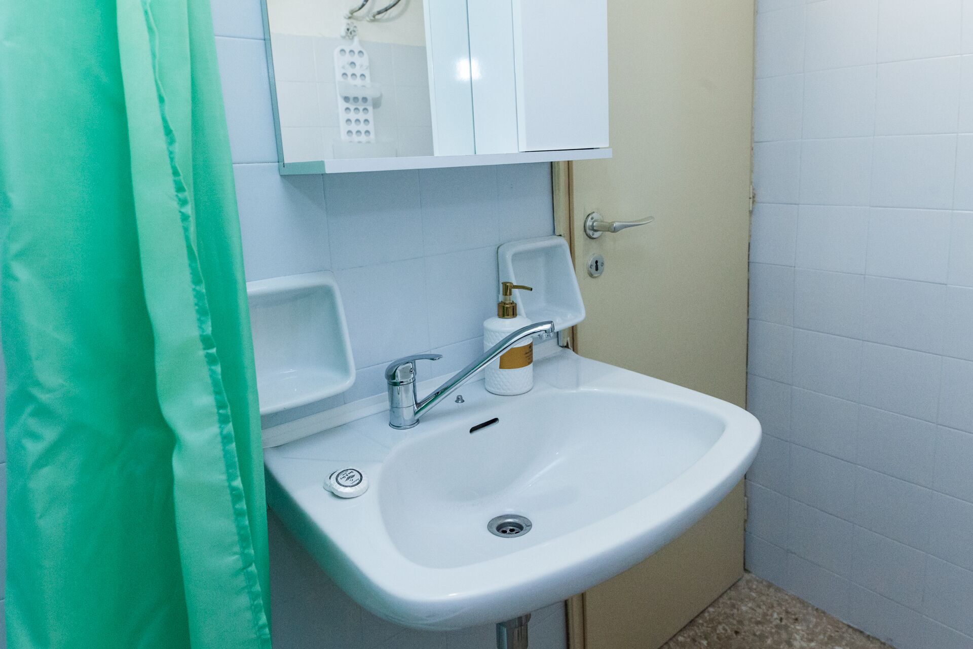 A bathroom with a white sink, a mirror, and a soap dispenser.