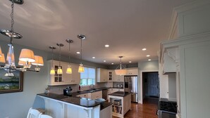 Une cuisine moderne avec des meubles blancs, un îlot central et des luminaires suspendus.