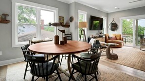 Un salon spacieux avec une table ronde en bois et des chaises, un canapé confortable et un téléviseur fixé au mur.