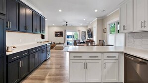 A modern kitchen with dark and white cabinetry, a central island, and a dining area with a view. - The Sand-Bar (Carolina Beach)