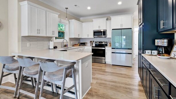A modern kitchen with white cabinetry, stainless steel appliances, and a central island with bar stools. - The Sand-Bar (Carolina Beach)