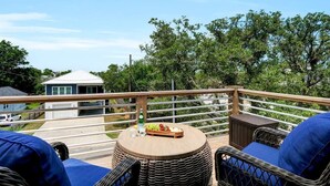 A balcony with wicker furniture, a round table, and a view of a house and trees. - The Sand-Bar (Carolina Beach)
