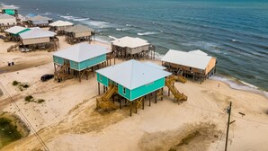 A coastal area with multiple wooden structures elevated on stilts over sandy terrain, likely serving as beach houses or cabins.