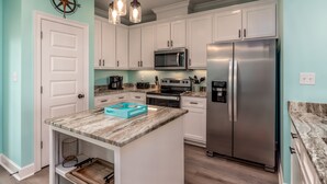 A modern kitchen with white cabinets, a stainless steel refrigerator, a built-in oven, and a microwave. There is a small island with a marble countertop and a blue tray.