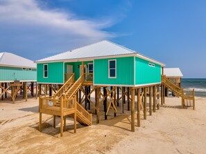 A turquoise beach house with wooden stairs and a metal roof, situated on stilts over the sand. - Simply Blessed - 106 Vargas Ct 4 Bedroom Home by RedAwning (Dauphin Island)