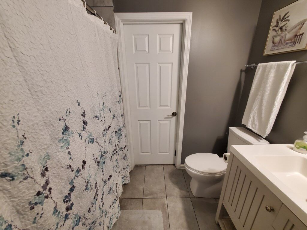 A bathroom with a white door, a toilet, and a sink with a towel hanging on the wall.