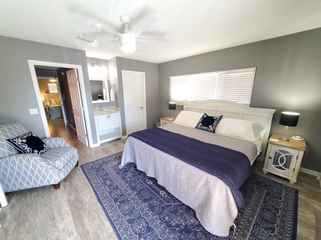 A bedroom with a bed, nightstands, a ceiling fan, a window with blinds, and a patterned rug.