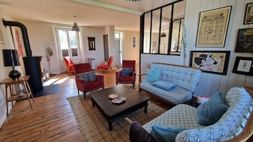 Un salón amplio con un sofá estampado, sillas rojas, una mesa de centro de madera y un ventanal grande.