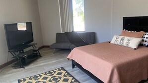 A bedroom with a bed, a television, a grey sofa, a patterned rug, and a window with blinds. - This casita is located in the Estrella neighborhood and boasts amazing View’s.  (Goodyear)