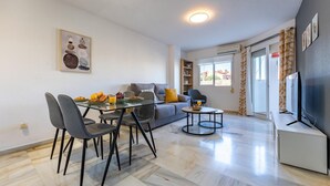 A modern living room with a glass dining table, grey sofa, and a TV stand.